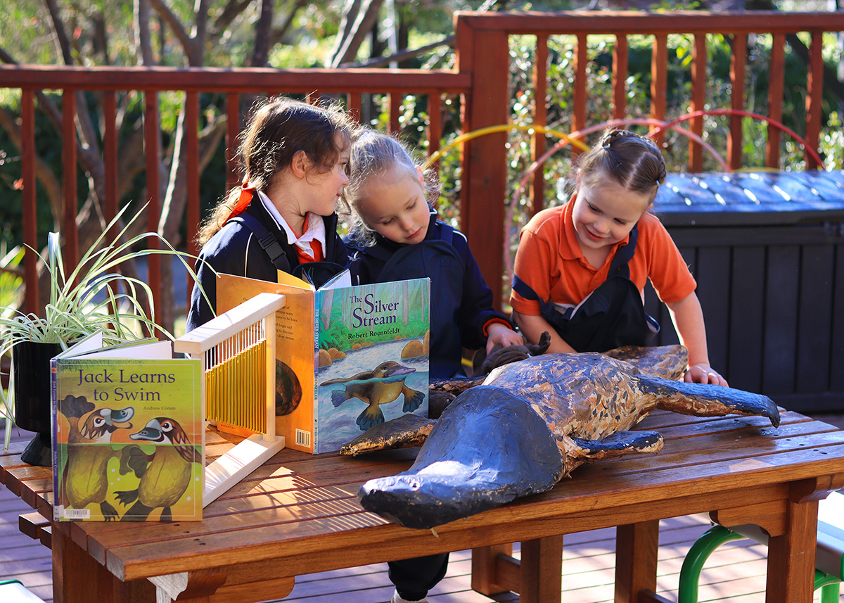 Junior School students exploring books and a platypus model outdoors